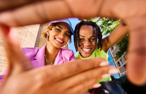 two gen z adults smiling and looking through a hand frame gesture outdoors in an urban environment. low angle shot. - fashion stock pictures, royalty-free photos & images