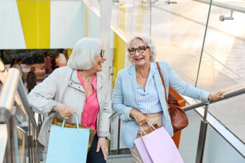 two senior women are walking up the stairs in a shopping mall while having fun shopping - fashion stock pictures, royalty-free photos & images