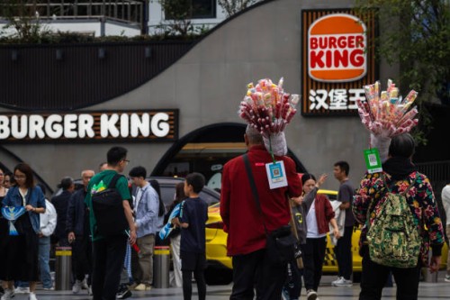 Two street vendors selling candied hawthorn walk past a Burger King restaurant during the National Day Golden Week holiday on October 5 in Chongqing,...