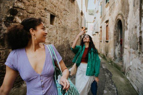 two stylish woman walk down an alleyway. one takes a photo using her mobile phone. - travel stock pictures, royalty-free photos & images