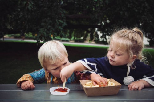 two toddlers sharing hot chips and tomato sauce at a picnic in the park - junk food stock pictures, royalty-free photos & images