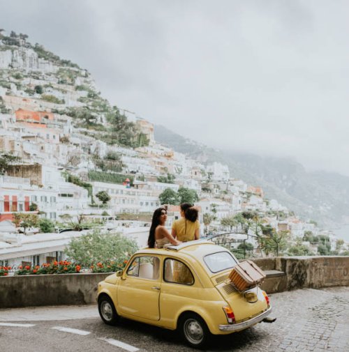 two woman stand in a vintage yellow fiat, and admire the view of positano, italy. - travel stock-fotos und bilder
