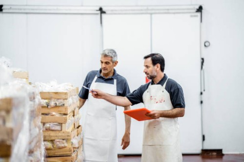 two workers taking inventory of packaged meat wooden boxes in warehouse - food stockfoto's en -beelden