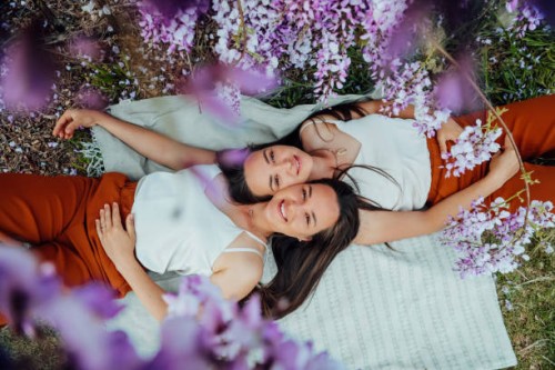 two young european twins with long dark hair lying on a picnic looking at the camera smiling faces close to each other top view through wisteria flowers - fashion stock pictures, royalty-free photos & images