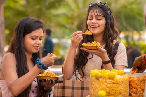 two young female friends eating indian street food (bhelpuri) at street market. - junk food stock pictures, royalty-free photos & images