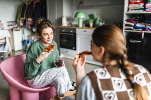 two young housemates eat pizza they ordered from outside together at home - junk food stock pictures, royalty-free photos & images