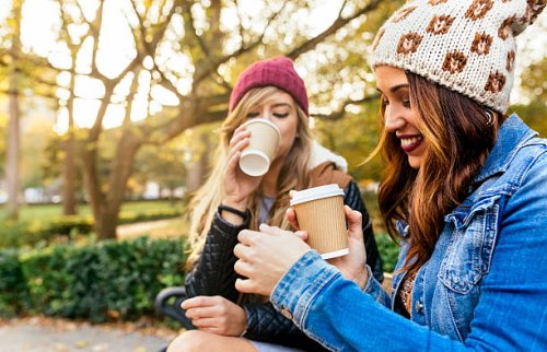 two young women drinking coffee in a park in autumn - junk food stock pictures, royalty-free photos & images