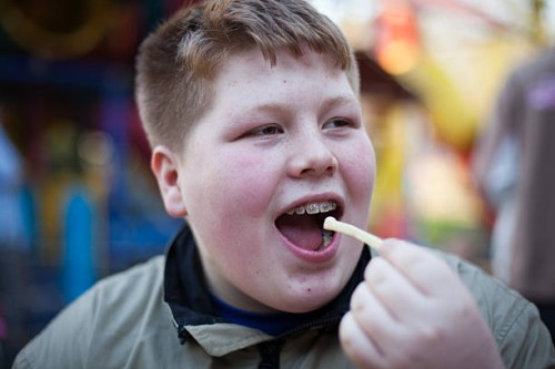 unhealthy eating: redhead overweight teenage boy eats french fries - junk food stock pictures, royalty-free photos & images