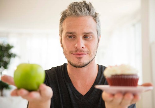 usa, new jersey, jersey city, man weighing green apple against cup cake - junk food stock pictures, royalty-free photos & images