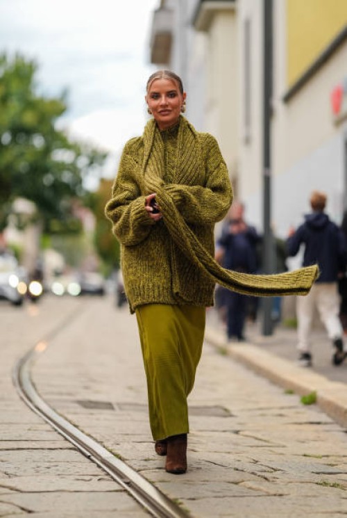 Veronica Ferraro wears gold earrings, dark green cotton knit oversized sweater, dark green cotton knit, dark green cotton knit oversized scarf, dark...