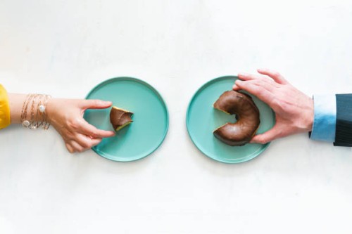 view from above of a woman's hand and a man's hand holding up two different sized pieces of a chocolate bun. concept of labor inequality. - junk food stock pictures, royalty-free photos & images