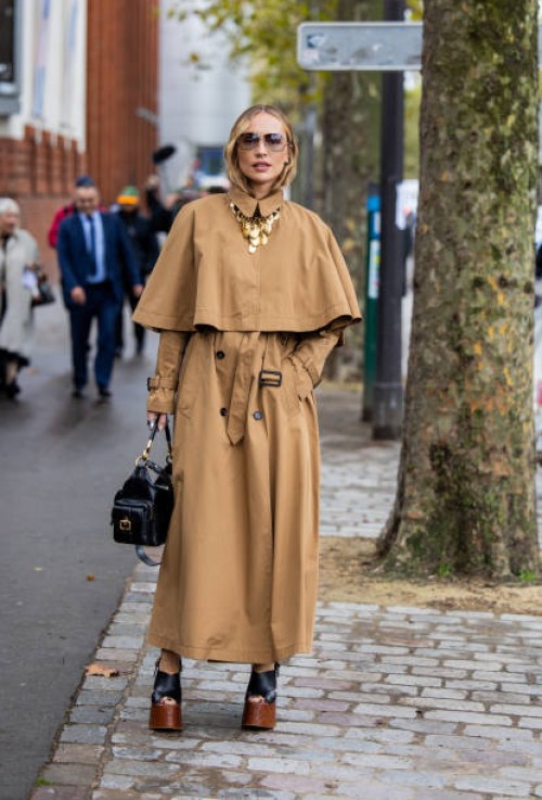 Viktoria Rader wears brown cape, trench coat, black bag, heeled shoes outside Chloe during Womenswear Spring/Summer 2025 as part of Paris Fashion...