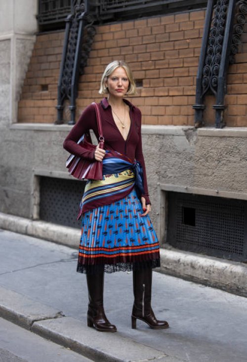 Violet Grace Atkinson wears burgundy cardigan, bag, wrapped scarf, blue laced black skirt, boots outside Lacoste during Womenswear Spring/Summer 2025...