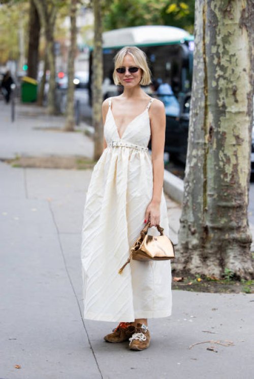 Violet Grace Atkinson wears creme white dress, metallic bag outside Ganni during Womenswear Spring/Summer 2025 as part of Paris Fashion Week on...