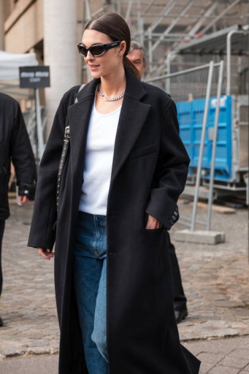 Vittoria Ceretti wears white tank top, blue jeans, black long coat, black loafers, black Balenciaga sunglasses, outside Miu Miu, during the...
