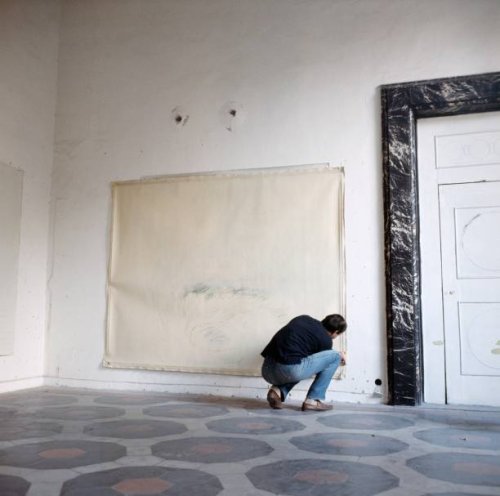 Vogue, November 15, 1966 - Artist Cy Twombly squatting to nail a large canvas on the wall in his apartment in a palazzo in Rome.