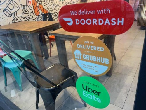 We Deliver, Doordash, Grubhub and Uber Eats signs on restaurant door, New York City.