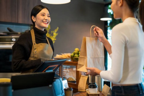 we hope you enjoy your drink of coffee. female cafe owner giving a take-out coffee to her customer at a cashier counter of a coffee shop. take-out food, point of sale system. - junk food stock pictures, royalty-free photos &