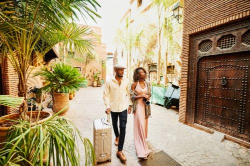 wide shot of couple arriving in hotel courtyard with rolling luggage - travel stock pictures, royalty-free photos & images