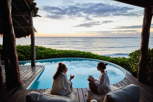 wide shot of female friends in discussion while sitting poolside at luxury suite of tropical resort at sunrise - travel stock pictures, royalty-free photos & images