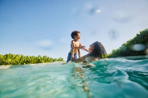 wide shot of laughing mother and son playing in pool at tropical resort - travel stock pictures, royalty-free photos & images