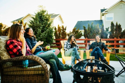 wide shot of smiling and laughing female friends hanging out by fire in backyard - garden decoration photos et images de collection