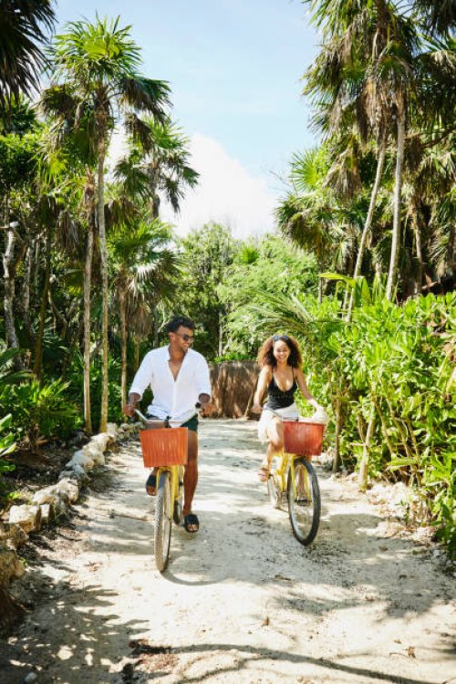 wide shot of smiling couple riding bikes to beach at tropical resort - travel stock pictures, royalty-free photos & images