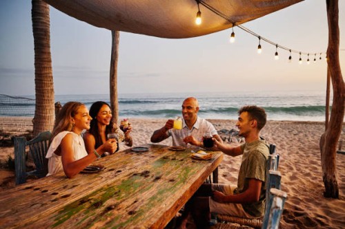 wide shot of smiling family enjoying drinks at tropical beach restaurant - travel stock pictures, royalty-free photos & images