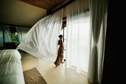 wide shot of woman standing in luxury hotel suite looking at view with curtains blowing in wind - travel stock pictures, royalty-free photos & images
