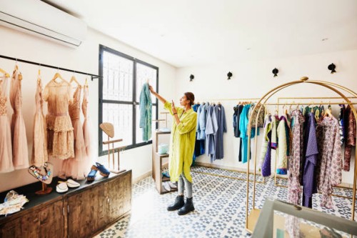 wide shot of woman taking photo of coat while shopping in boutique - fashion stock pictures, royalty-free photos & images