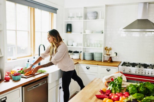 wide shot of woman washing fresh produce in kitchen sink after grocery shopping - fashion stock pictures, royalty-free photos & images