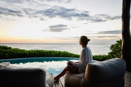 wide shot of woman watching sunrise while sitting poolside at luxury suite at tropical resort - travel stock-fotos und bilder