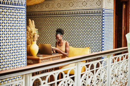 wide shot woman working on laptop in alcove of ornately decorated riad - travel stockfoto's en -beelden