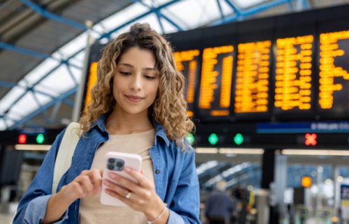 woman at the train station using her phone while checking the departure board - travel stock pictures, royalty-free photos & images