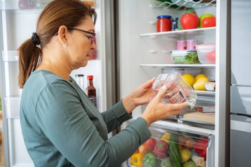 woman by the fridge reading label of refrigerated food package - food stock pictures, royalty-free photos & images