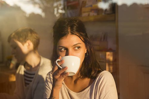woman drinking coffee in urban cafe while looking outside, sunny reflections in window. - coffee stock pictures, royalty-free photos & images