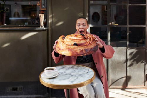 woman eating large raisin roll while sitting at sidewalk cafe - junk food stock-fotos und bilder