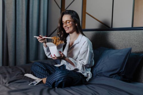 woman eating pasta and watching movie at bed at night - junk food stock pictures, royalty-free photos & images