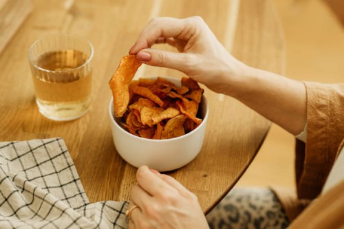 woman eating sweet potato chips snacks close up of hands and bowl - junk food stock pictures, royalty-free photos & images