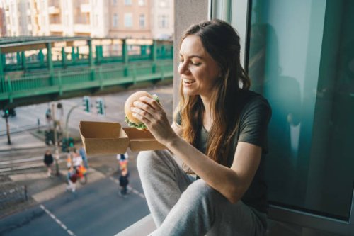 woman eating take out burger at home in front of the open window - junk food stock pictures, royalty-free photos & images