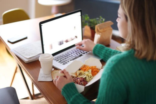woman eating takeaway food while working on her laptop - junk food stock pictures, royalty-free photos & images