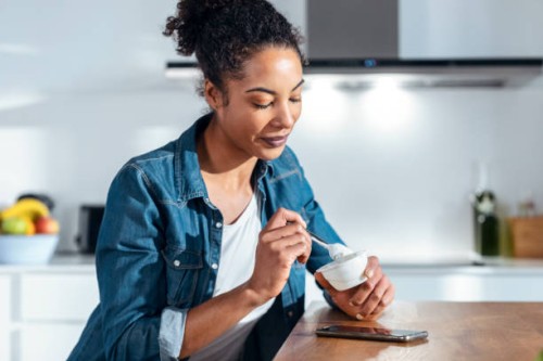 woman eating yogurt sitting in kitchen at home - food stock pictures, royalty-free photos & images