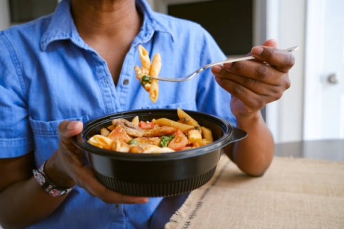 woman eats takeout pasta and chicken dish - junk food stock pictures, royalty-free photos & images