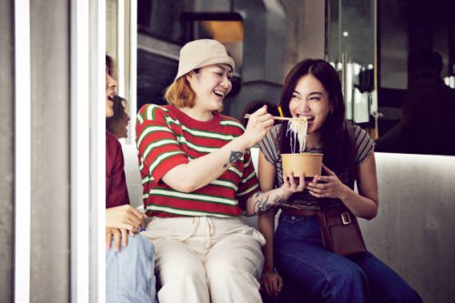 woman feeding noodles to female friend - junk food stock pictures, royalty-free photos & images
