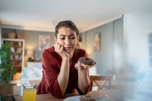 woman feeling guilty while eating chocolate donut at home - junk food stock pictures, royalty-free photos & images