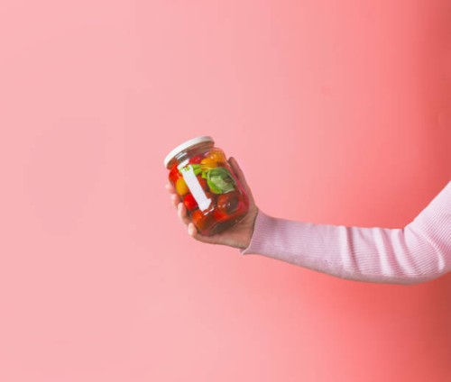 woman hands with light pink sweatshirt holding glass jar with various preserved food on pink background - food stock pictures, royalty-free photos & images