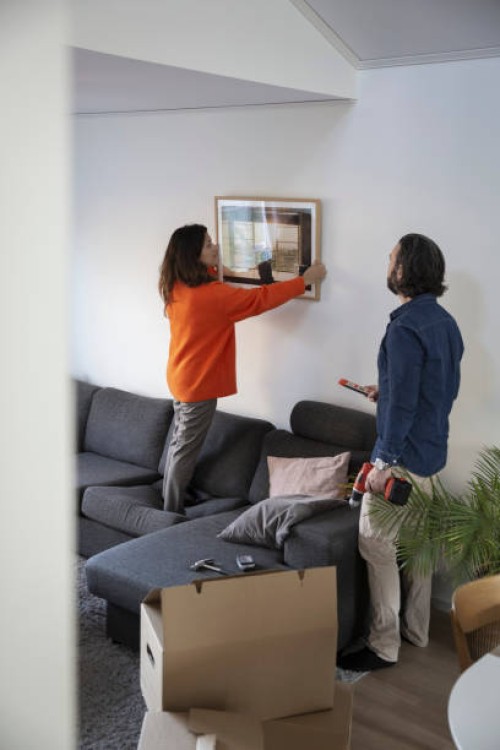 woman hanging picture frame on wall by man in living room - home decoration stock pictures, royalty-free photos & images