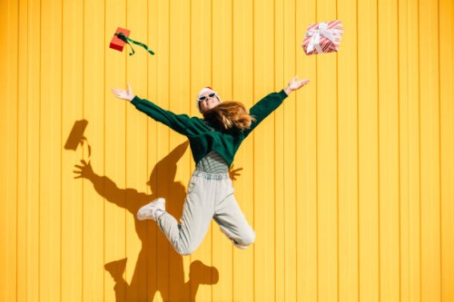 woman in christmas hat and green sweater jumping with christmas gift box against the yellow wall. - fashion stock pictures, royalty-free photos & images