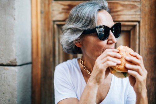 woman in sunglasses eating burger while sitting against door - junk food stock pictures, royalty-free photos & images