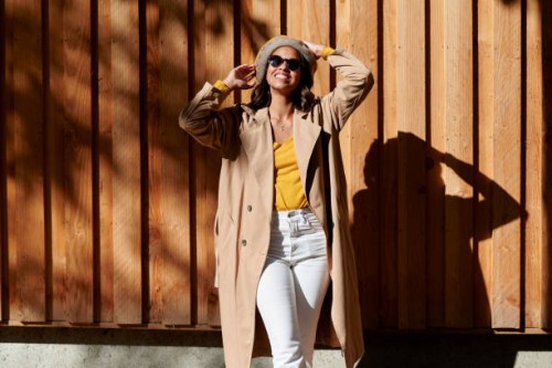 woman in trench coat raising arms in front of wooden wall - fashion stock-fotos und bilder